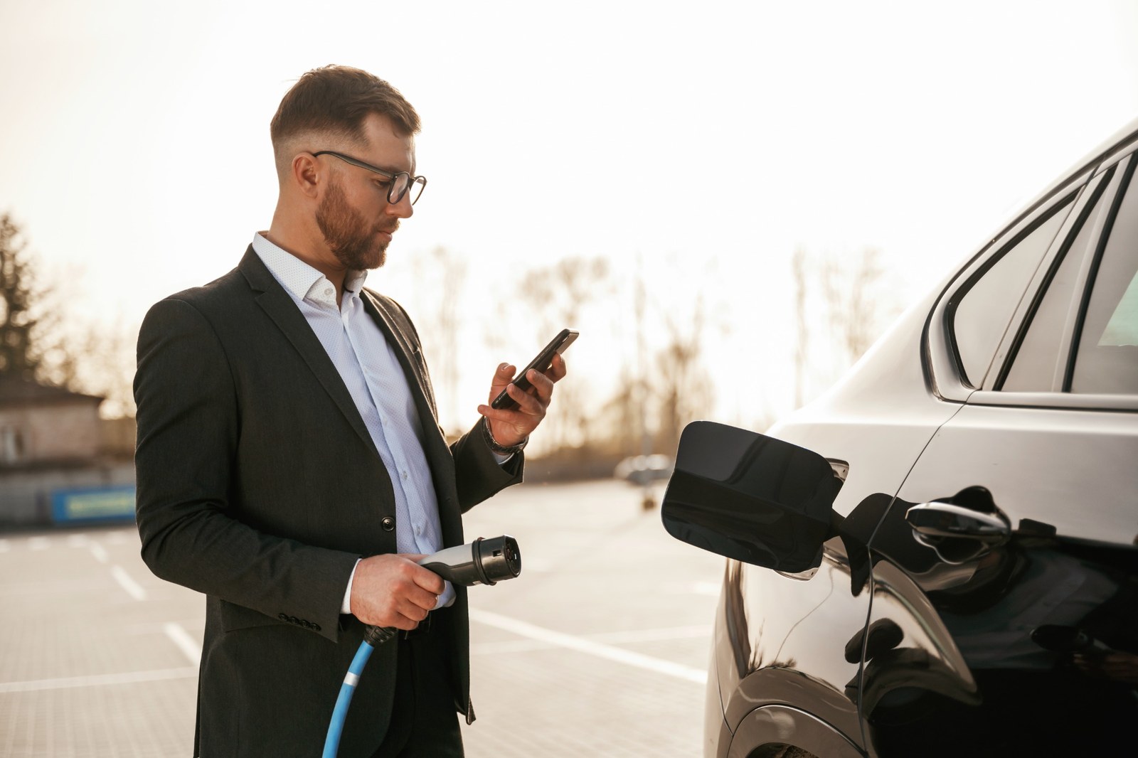 Un utilisateur consulte son smartphone près d’une voiture électrique en recharge