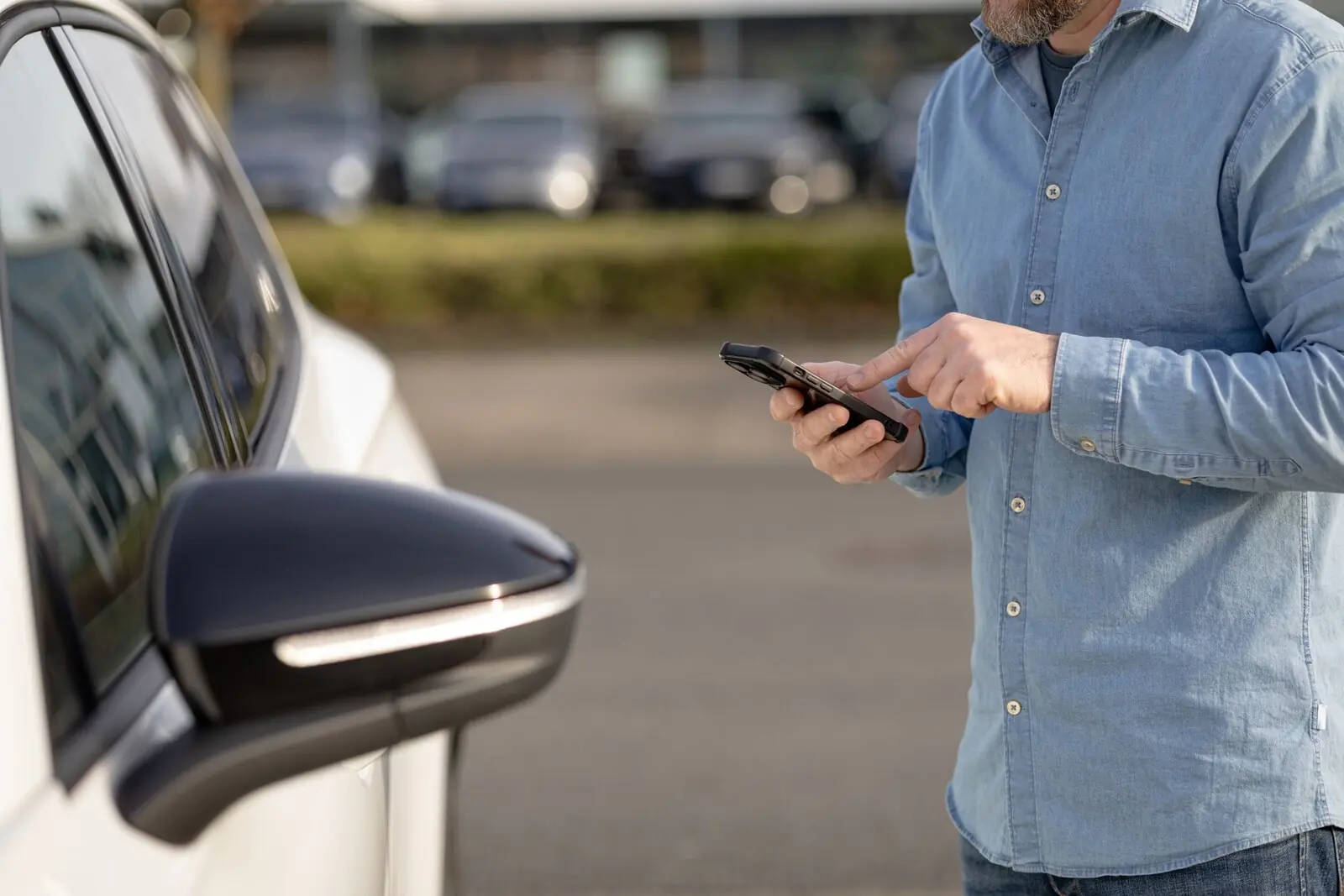 Un utilisateur consulte son smartphone à proximité de la portière d’une voiture.