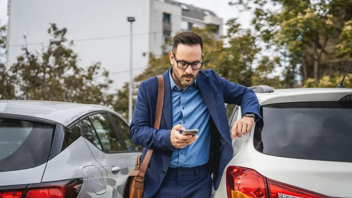 Un professionnel consulte son smartphone entre deux véhicules sur un parking.